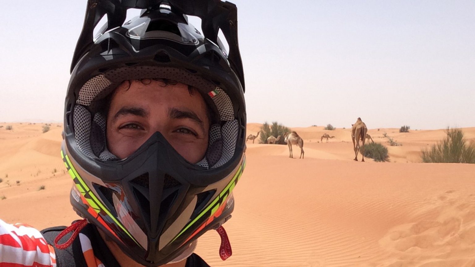 Daniel Ricciardo a sivatagban, háttérben tevékkel