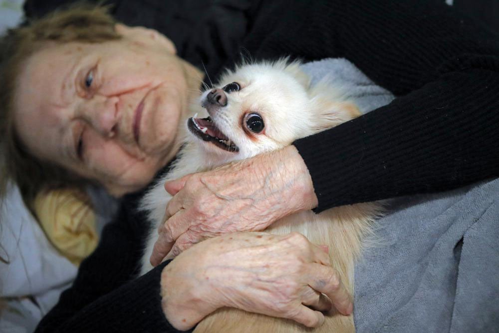Kutyáját ölelő nő egy romániai bálteremben, melyet ideiglenes menekültházzá alakítottak