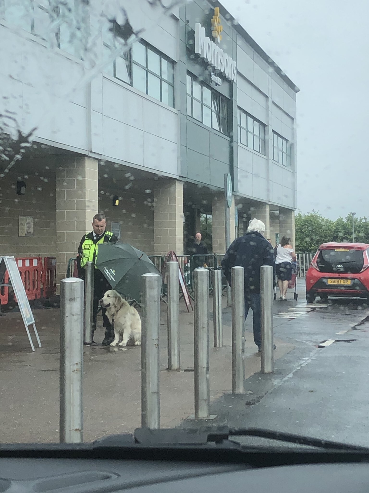 Emberség: ernyőt tartott a türelmesen várakozó kutya fölé az esőben egy biztonsági őr